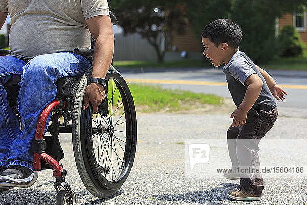 Hispanoamerikanischer Mann mit Rückenmarksverletzung im Rollstuhl spielt mit seinem Sohn