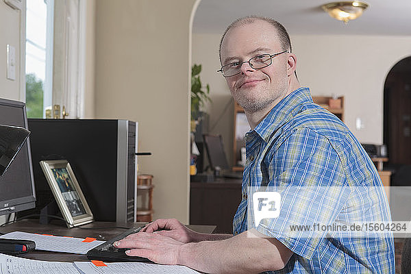 Mann mit Down-Syndrom bei der Arbeit an einem Computer in einem Büro