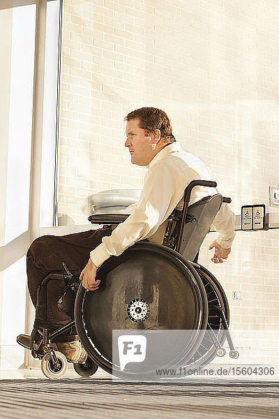 Geschäftsmann mit Querschnittslähmung im Rollstuhl benutzt den automatischen Türöffner am Eingang eines Bürogebäudes