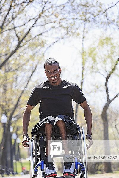 Mann im Rollstuhl,  der an Spinaler Meningitis erkrankt ist,  geht durch einen Park