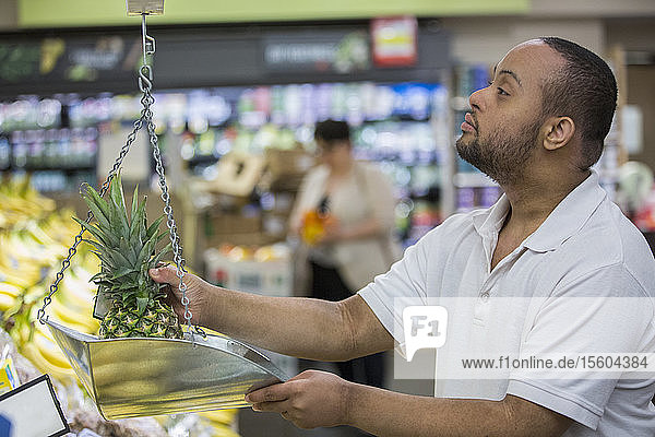 Mann mit Down-Syndrom beim Wiegen von Ananas in einem Lebensmittelladen