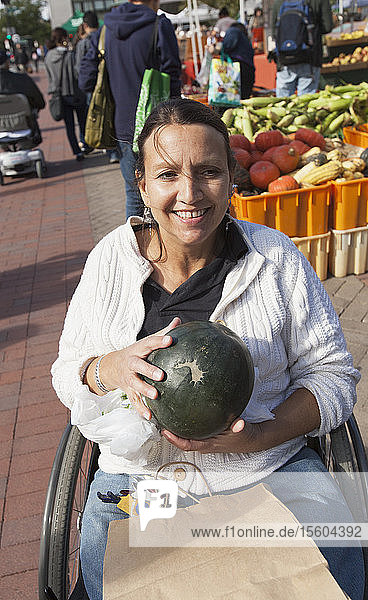 Frau mit Querschnittslähmung sitzt im Rollstuhl und kauft auf einem Markt Wassermelonen ein