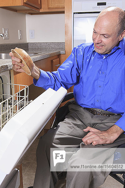 Mann mit Friedreich-Ataxie und deformierten Händen bei der Benutzung seiner Spülmaschine
