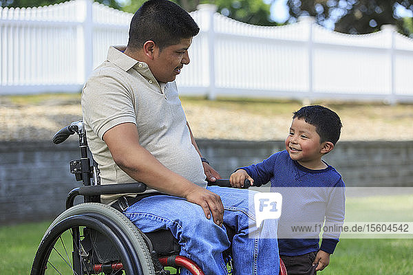 Hispanic man with Spinal Cord Injury in wheelchair with his son in lawn