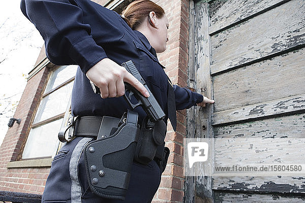 Eine Polizistin steht mit einer Pistole vor der Tür.