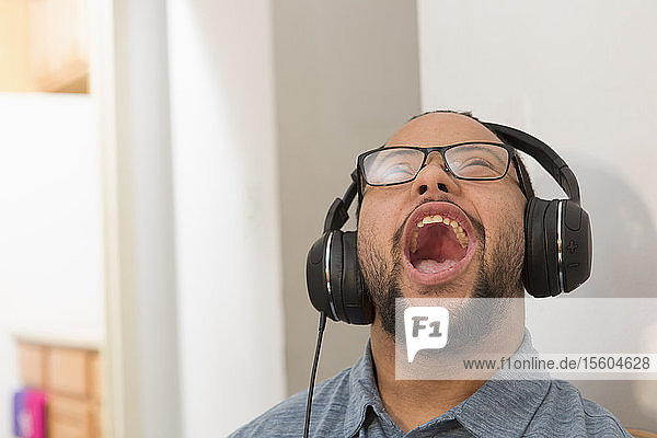 Glücklicher afroamerikanischer Mann mit Down-Syndrom  der zu Hause mit Kopfhörern Musik hört und singt