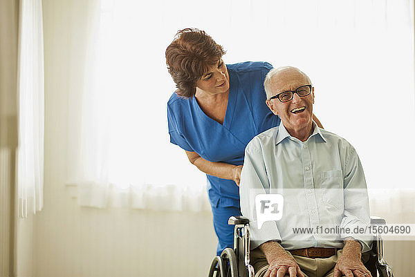 Porträt eines lächelnden älteren Mannes  der von einer Krankenschwester getröstet wird  während er in einem Rollstuhl sitzt