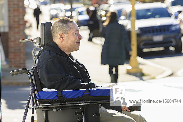 Mann mit Rückenmarksverletzung und Arm mit Nervenschaden in motorisiertem Rollstuhl überquert öffentliche Straße
