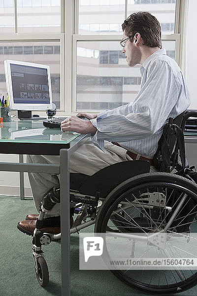 Mann im Rollstuhl mit einer Rückenmarksverletzung bei der Arbeit am Schreibtisch in einem Heimbüro