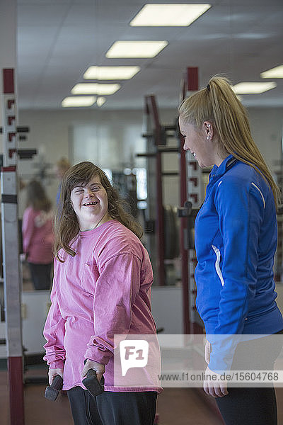 Junge Frau mit Down-Syndrom trainiert mit ihrem Trainer mit Gewichten im Fitnessstudio