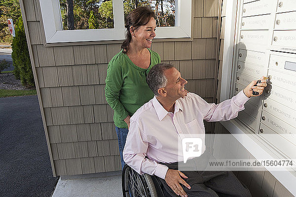 Mann im Rollstuhl mit Frau holt Post aus dem Briefkasten ihrer neuen Wohnung