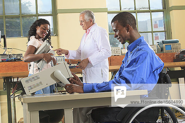 Professor und Ingenieurstudenten in einem Elektronik-Klassenzimmer  einer im Rollstuhl bei der Vorbereitung eines Oszilloskops für das Labor