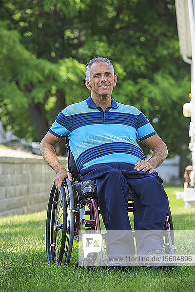 Porträt eines glücklichen Mannes mit einer Rückenmarksverletzung im Rollstuhl auf einer Wiese