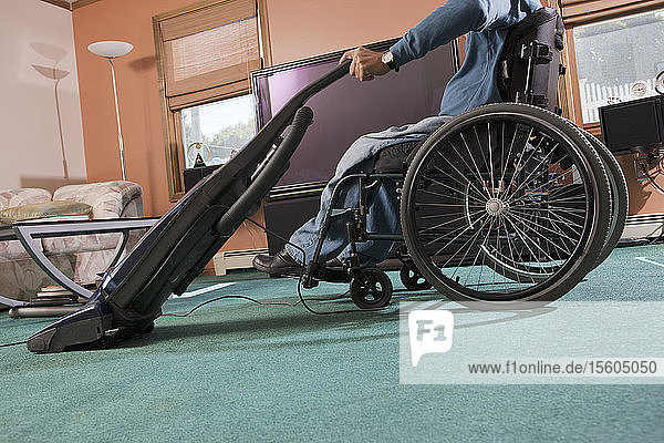 Mann mit Querschnittslähmung im Rollstuhl benutzt zu Hause einen Staubsauger