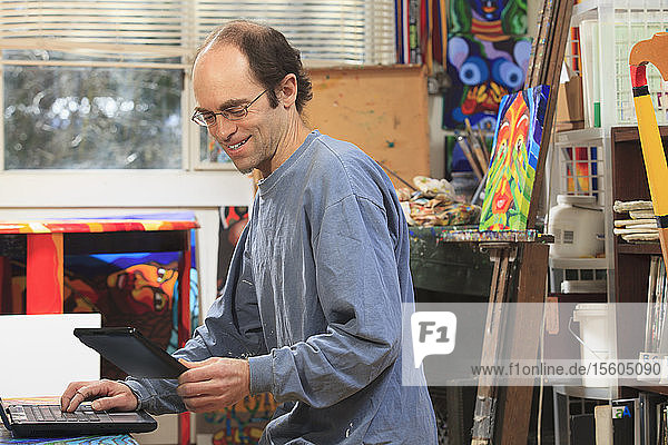 Mann mit Asperger-Syndrom bei der Arbeit an seinem Tablet und Computer in seinem Kunstatelier