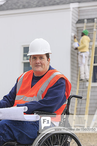 Construction engineer with spinal cord injury with house plans at construction site