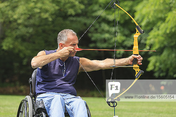 Man with spinal cord injury in wheelchair aiming his bow and arrow for archery practice