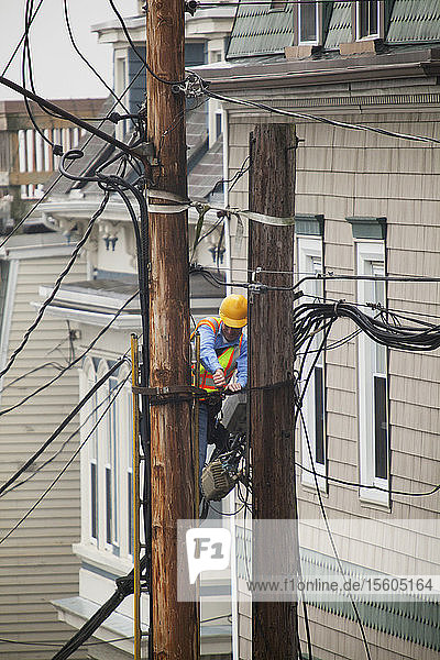 Cable lineman on ladder trimming wiring on city power poles
