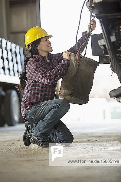 Female power engineer attaching canvas bucket to equipment truck