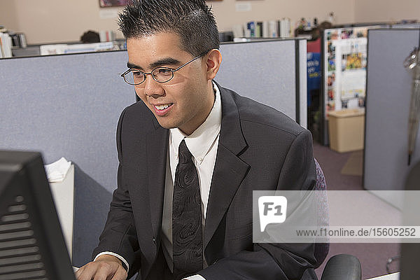 Glücklicher asiatischer Mann mit Autismus arbeitet am Computer in einem Büro