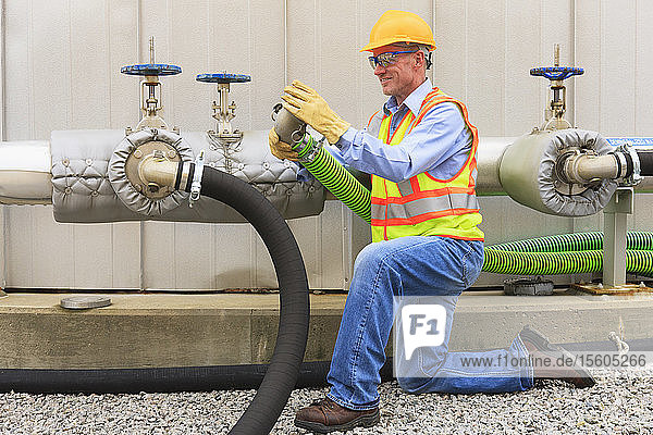 Engineer at electric power plant examining connection hose near water storage tank
