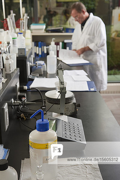 Flasks and reagent bottles on a laboratory bench with a scientist in the background