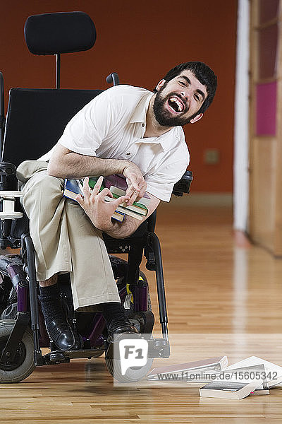 Portrait of a mid adult man sitting in a wheelchair holding books and laughing