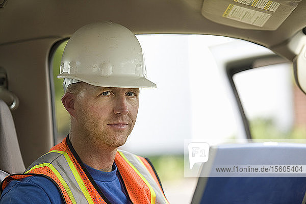 Porträt eines Bauarbeiters  der einen Laptop in einem Lastwagen benutzt