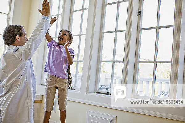 Lächelndes junges Mädchen gibt ihrem Arzt die Hand