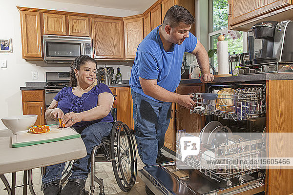 Frau mit Spina Bifida und ihr Mann benutzen den Geschirrspüler in der Küche