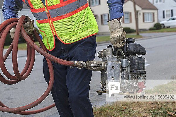 Techniker der Wasserbehörde trägt eine benzinbetriebene Pumpe zum Spülen von Hydranten