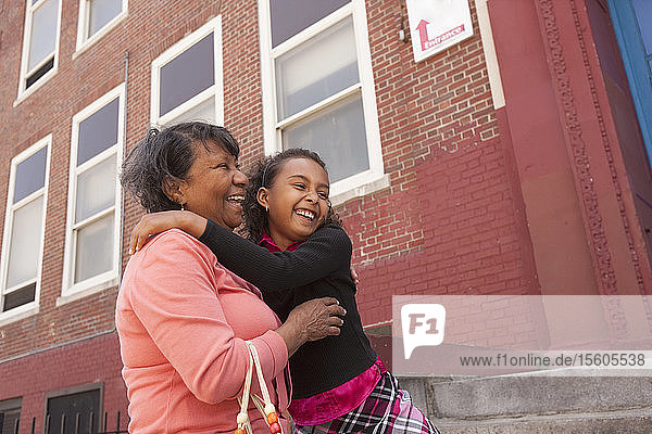 Hispanisches Mädchen lächelt mit ihrer Großmutter vor einem Bildungsgebäude