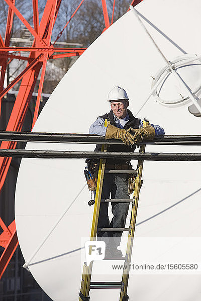 Kabelmonteur  der auf einer Leiter steht  um eine Übertragungsleitung zu reparieren