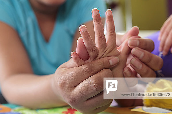 Mutter streckt die Hände ihrer kleinen Tochter mit zerebraler Lähmung
