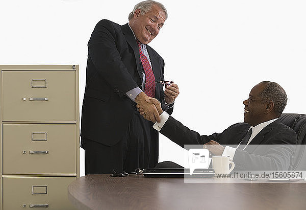Zwei Geschäftsleute schütteln sich die Hände und lächeln in einem Büro