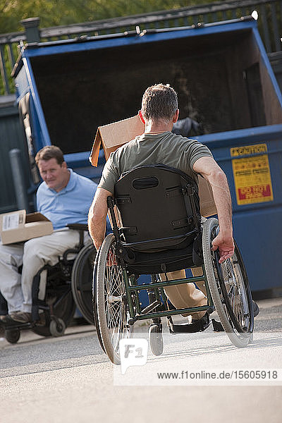 Männer in Rollstühlen mit Rückenmarksverletzungen bringen den Müll zur Mülltonne