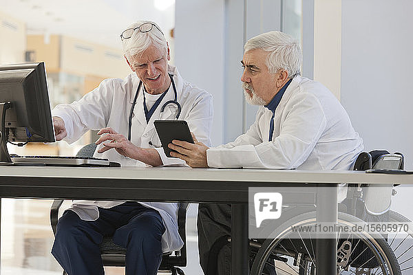 Arzt mit Muskeldystrophie im Rollstuhl im Gespräch mit einem anderen Arzt
