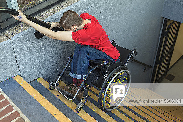 Trendiger Mann mit einer Rückenmarksverletzung im Rollstuhl  der rückwärts eine U-Bahn-Treppe hinunterfährt