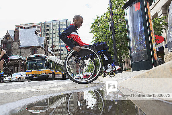 Mann im Rollstuhl  der an Spinaler Meningitis leidet  fährt über einen Bordstein