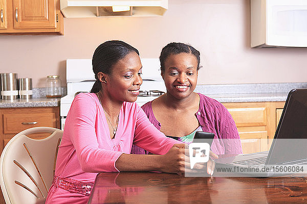 Zwei Schwestern arbeiten zu Hause mit Smartphone und Laptop  eine davon mit Lernbehinderung