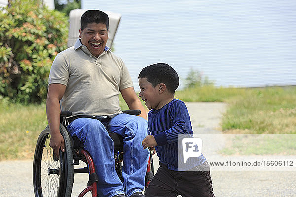 Hispanoamerikanischer Mann mit Rückenmarksverletzung im Rollstuhl spielt mit seinem Sohn