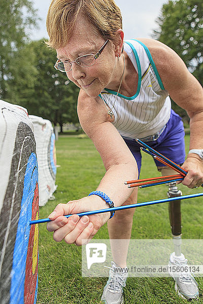 Woman with prosthetic leg pulling arrows from target after archery practice