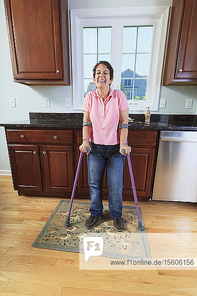 Frau mit zerebraler Lähmung benutzt ihre Krücken und lächelt in der Küche