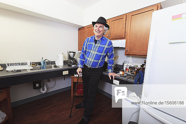 Mann mit Multipler Sklerose steht mit einem Stock in seiner barrierefreien Küche