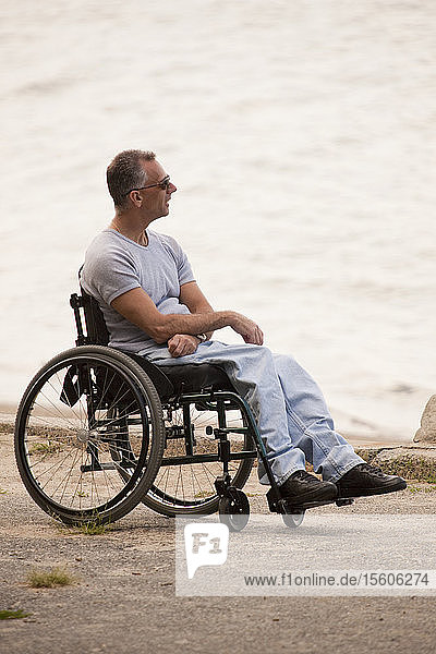 Mann mit Querschnittslähmung sitzt im Rollstuhl am Meer