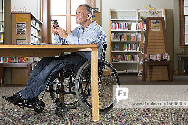 Mann mit Rückenmarksverletzung in einer Bibliothek  der sich eine DVD ansieht