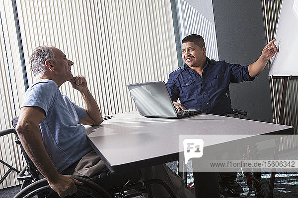Two men with Spinal Cord Injuries working with a presentation board in an office
