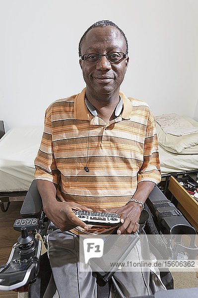 Mann mit Guillain-Barre-Syndrom benutzt seine Bluetooth-Mini-Tastatur in seinem elektrischen Rollstuhl zu Hause