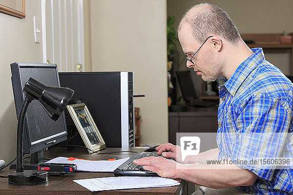 Mann mit Down-Syndrom bei der Arbeit an seinem Computer in einem Büro