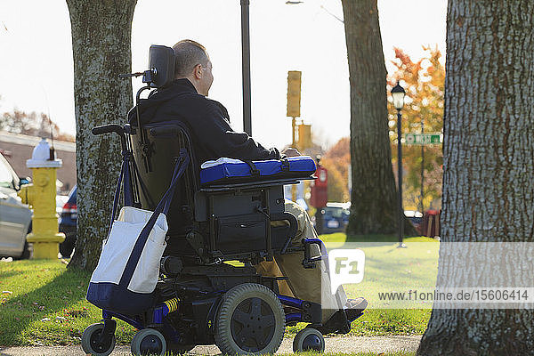 Mann mit Rückenmarksverletzung und Arm mit Nervenschaden im motorisierten Rollstuhl in einem öffentlichen Park